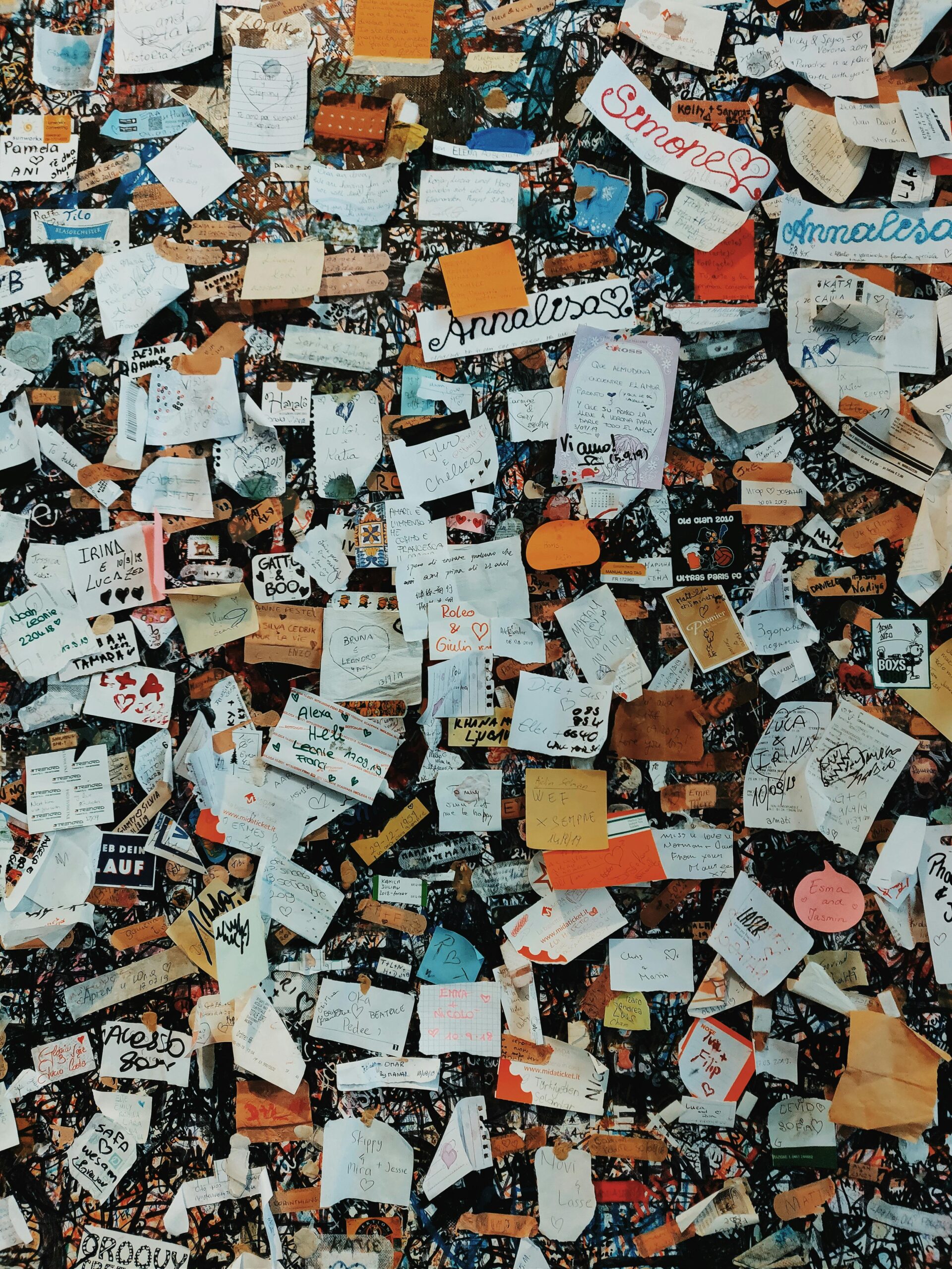 A vibrant collection of overlapping sticky notes and papers on a wall, showcasing messages and doodles.