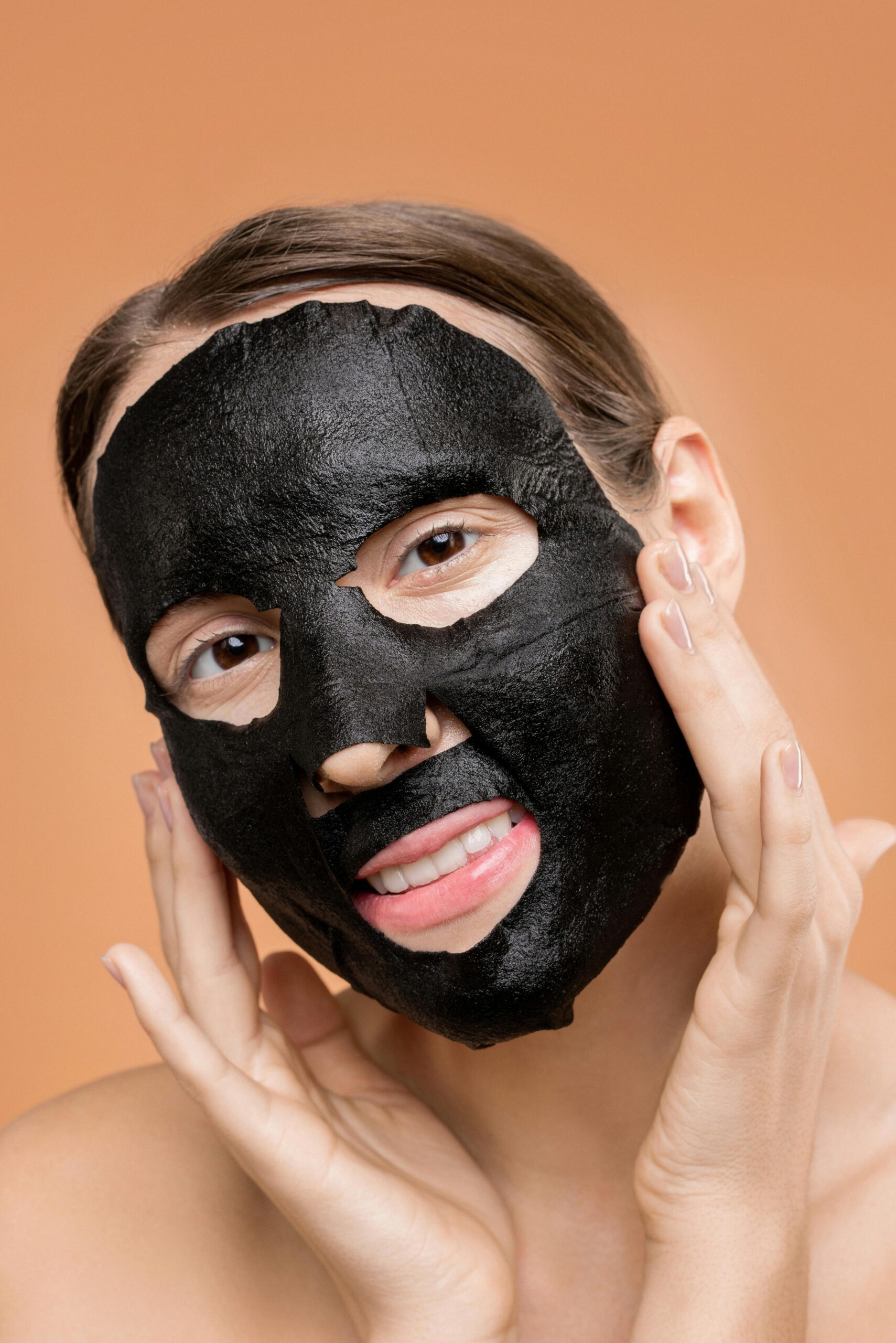 A woman with a black face mask smiles and touches her face, embodying skincare bliss.