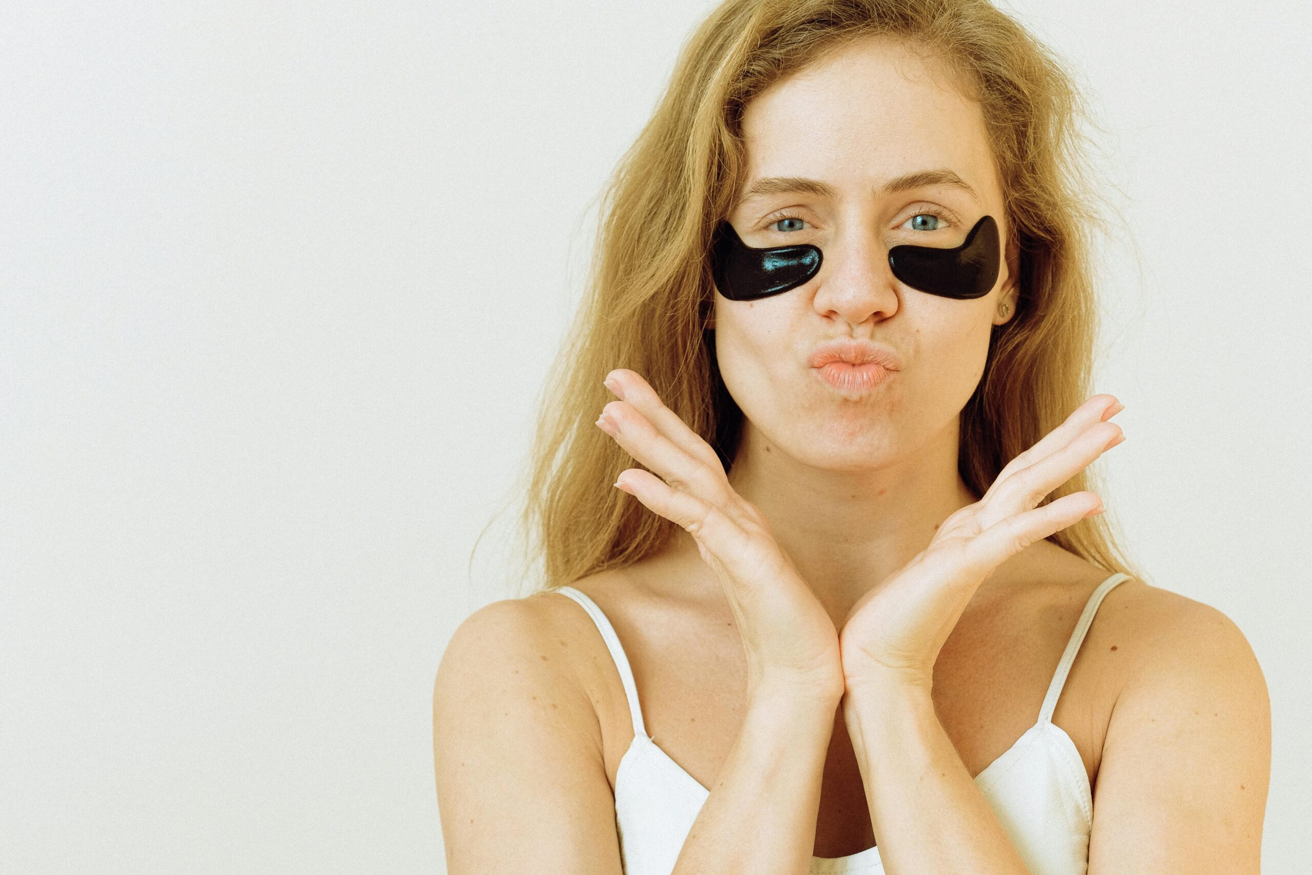 A woman poses playfully with black under-eye patches on a white background.