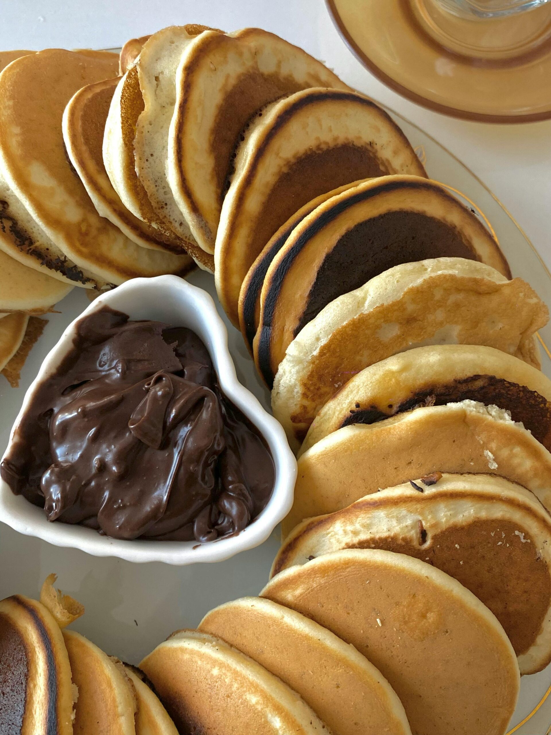 Delicious stack of pancakes with a side of rich chocolate spread on a plate.