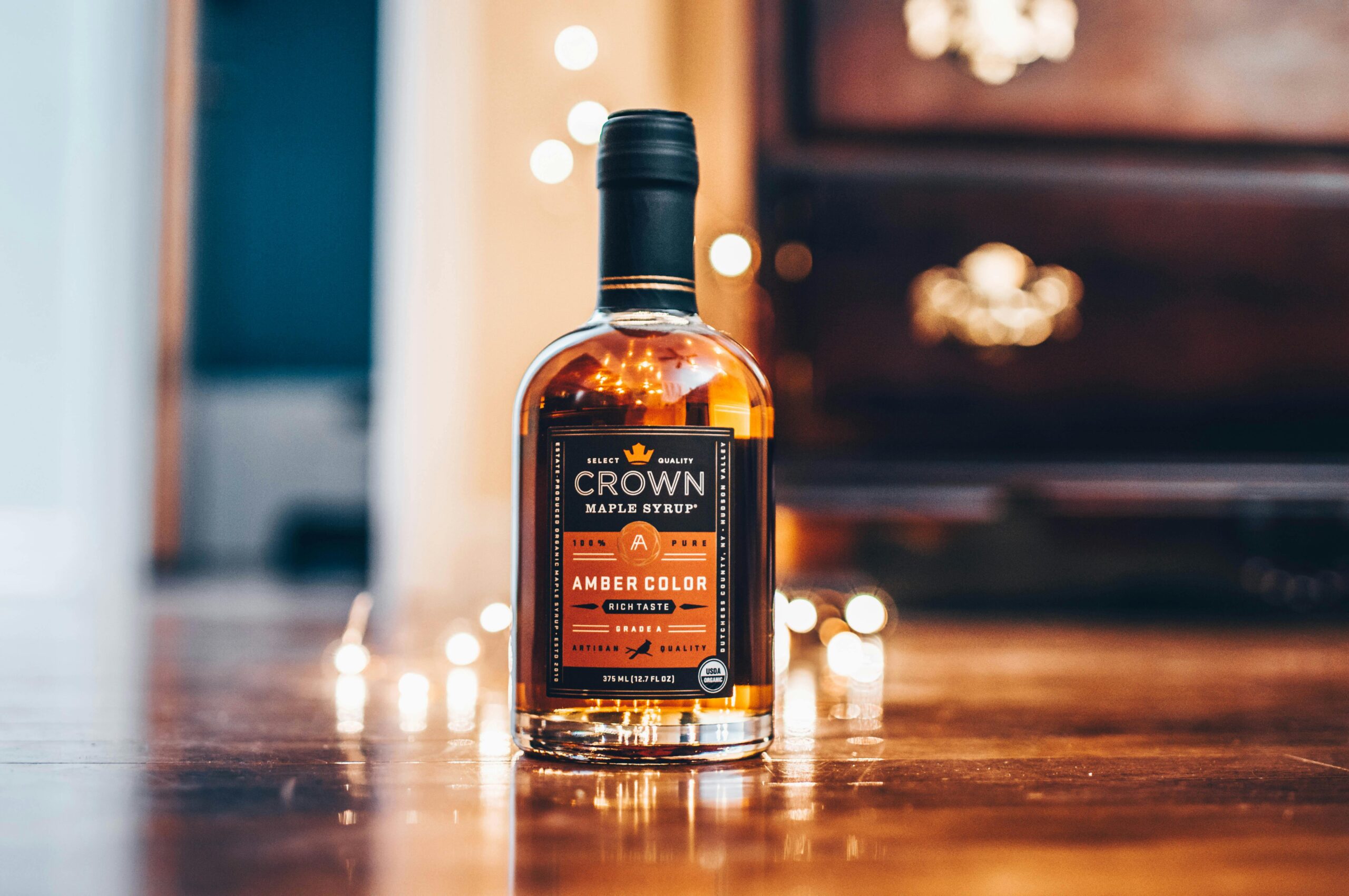 A close-up of a Crown maple syrup bottle showcasing rich amber color on a wooden surface.