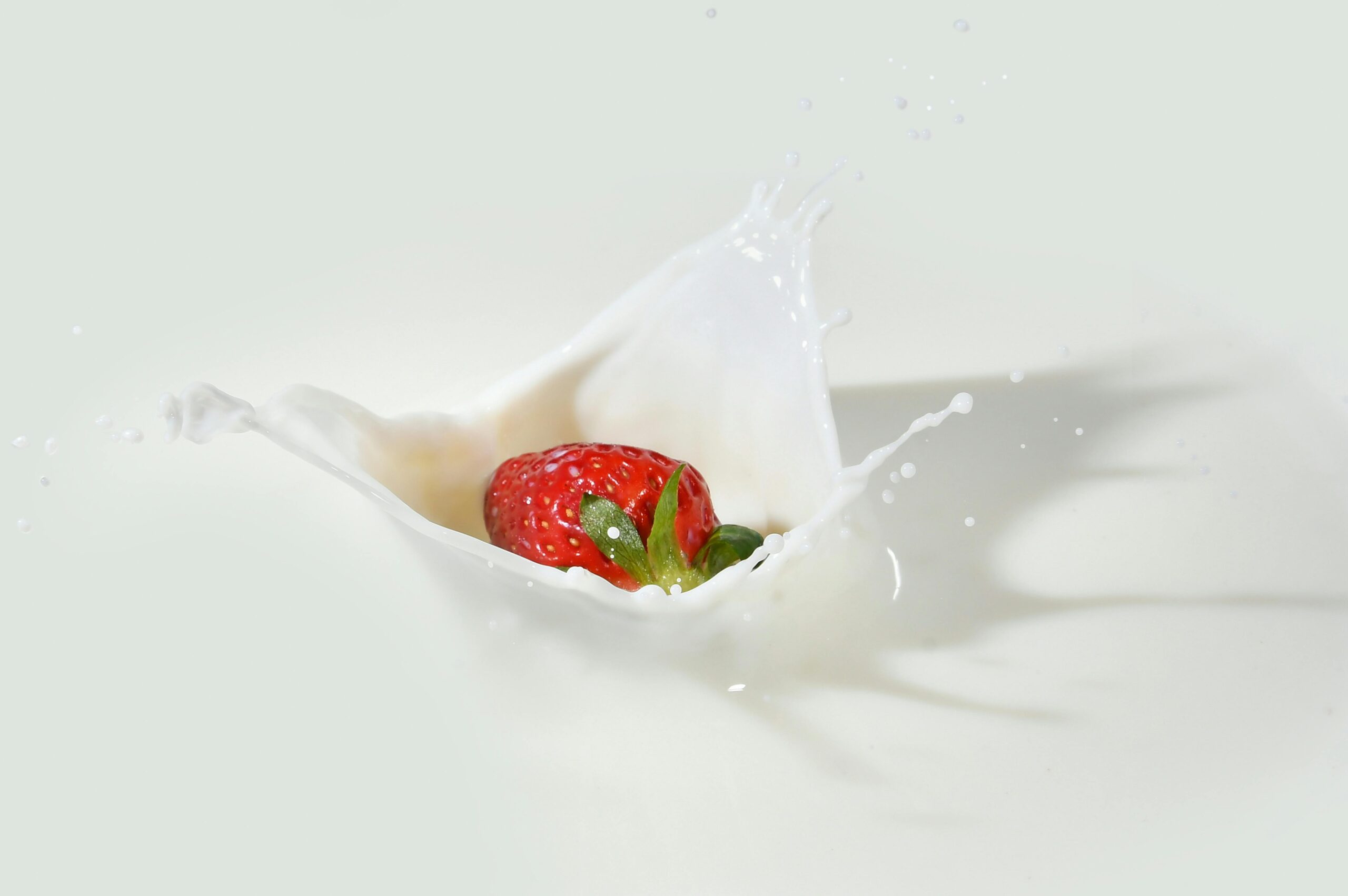 A vibrant strawberry makes a splash in creamy white milk, showcasing freshness and vivid colors.