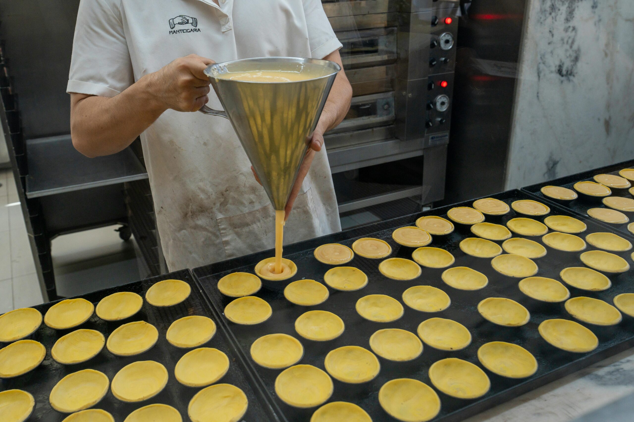 Baker fills pastry shells with custard for pastéis de nata in a Portuguese bakery.