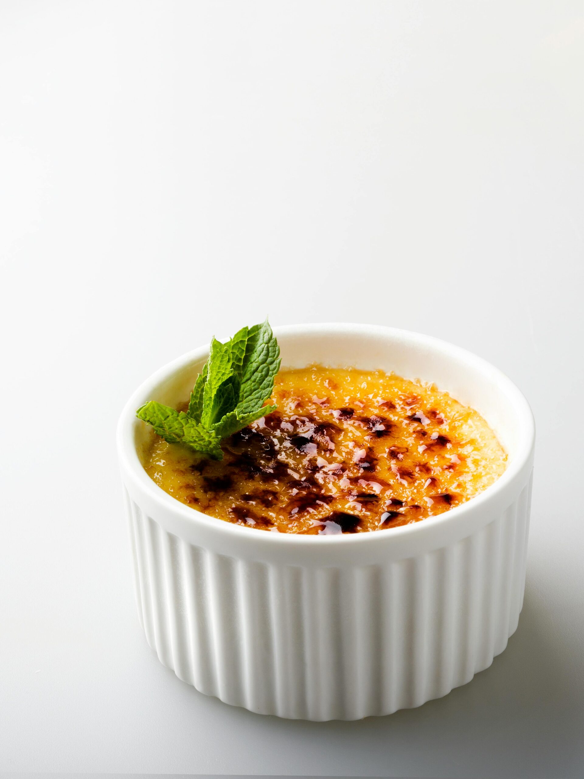 Close-up of a delicious crème brûlée topped with mint, set against a white background.