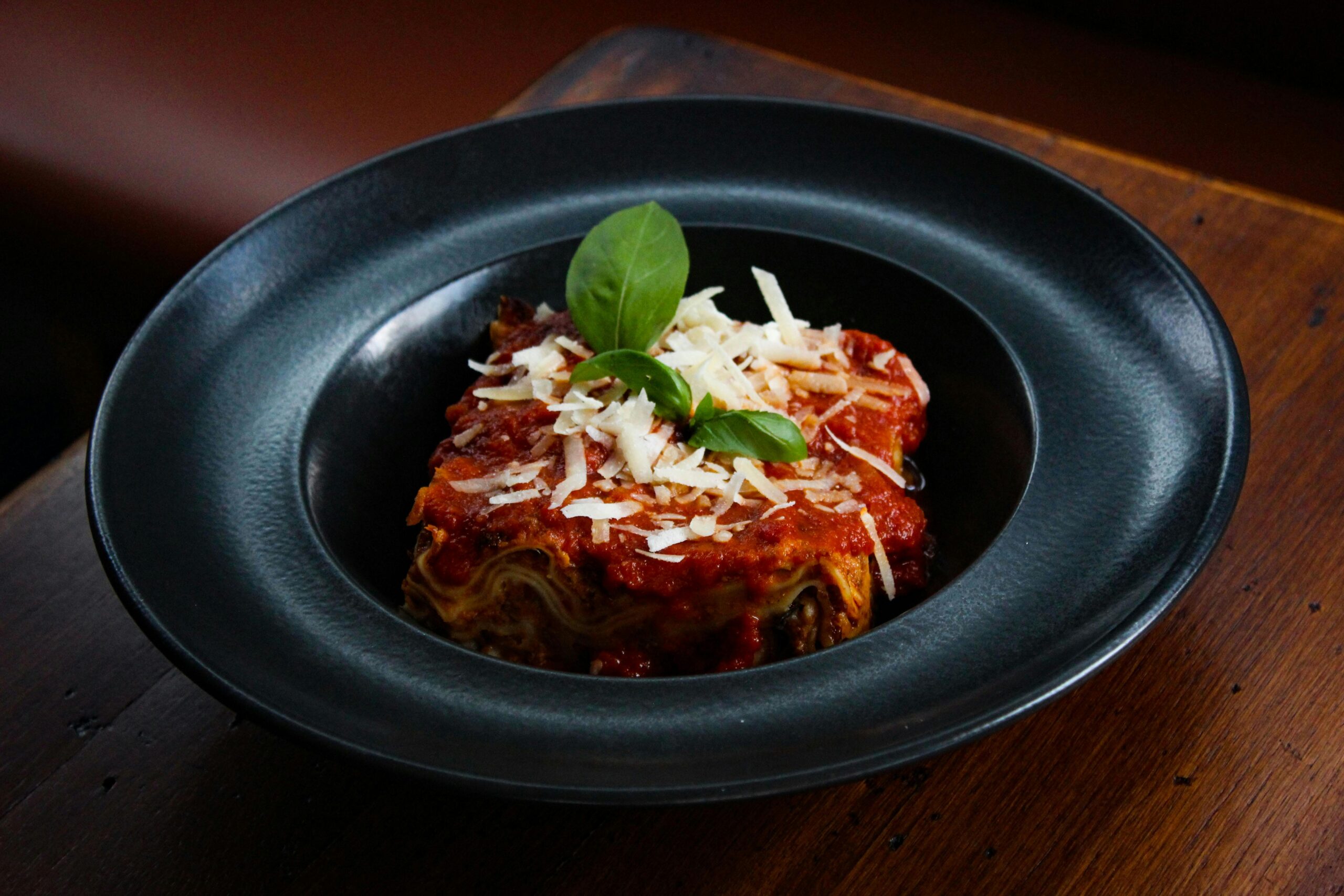 Close-up of a delicious lasagna served in a black plate, garnished with cheese and basil.