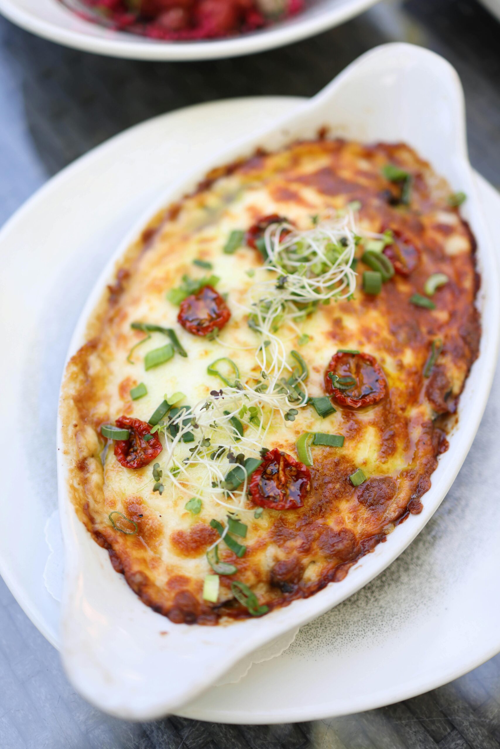 Close-up of a baked pasta dish topped with melted cheese, herbs, and sundried tomatoes.