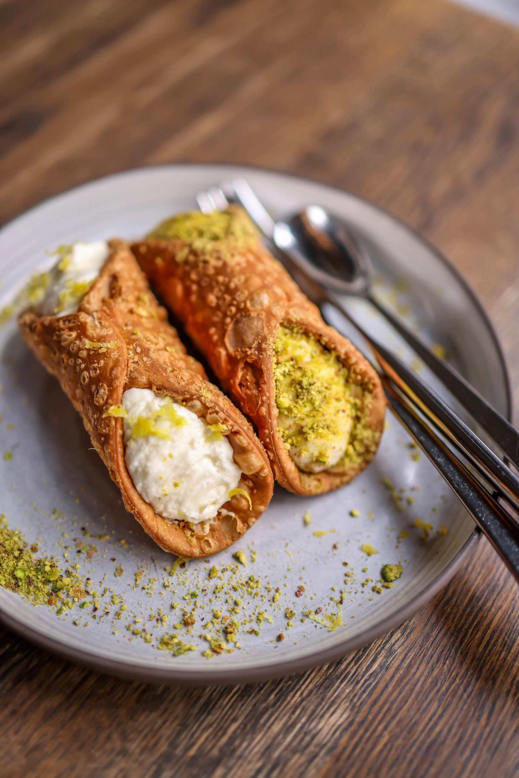 Close-up of two crispy cannoli on a plate filled with ricotta and topped with pistachios.