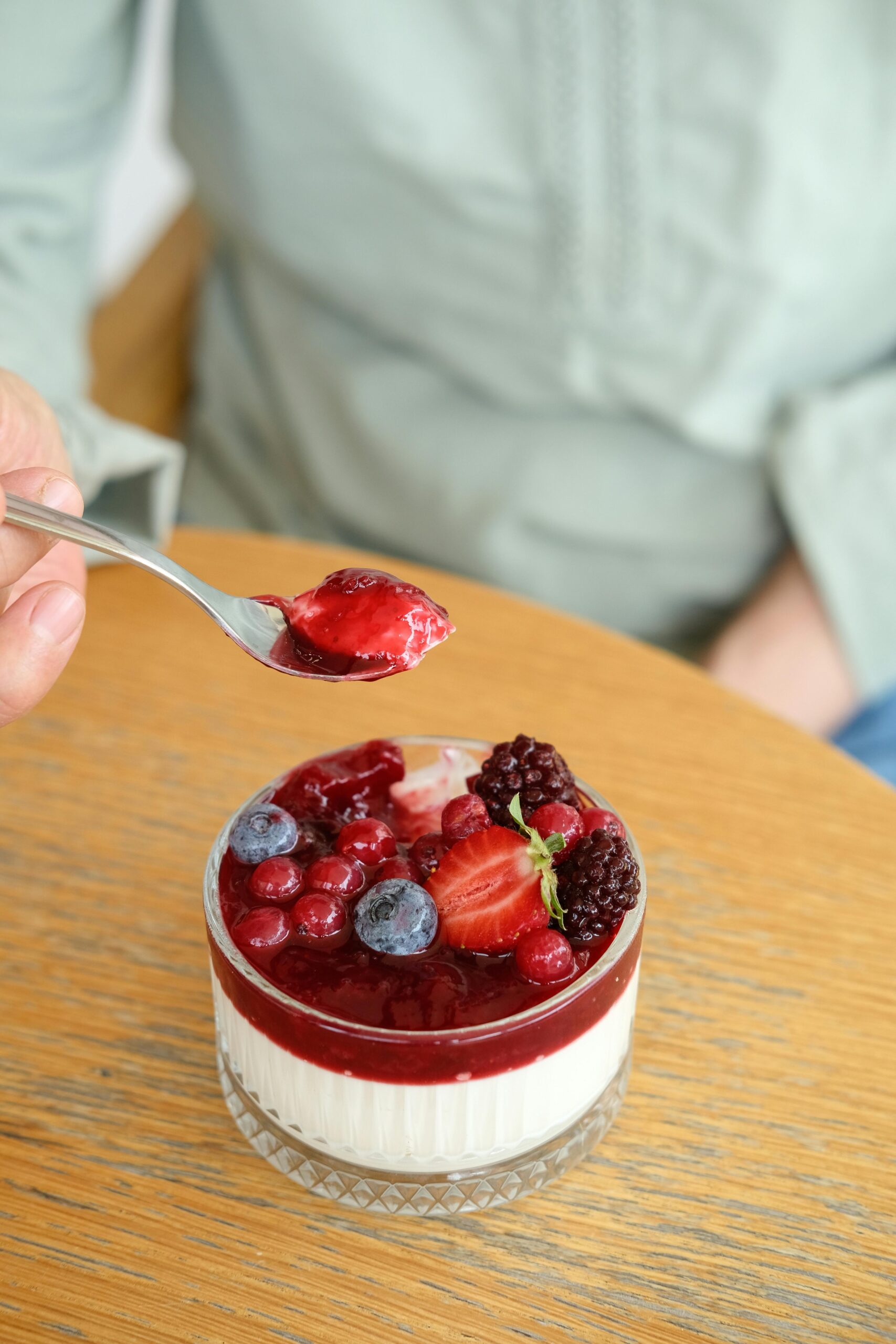 Close-up of a creamy yogurt dessert topped with berries being enjoyed indoors.