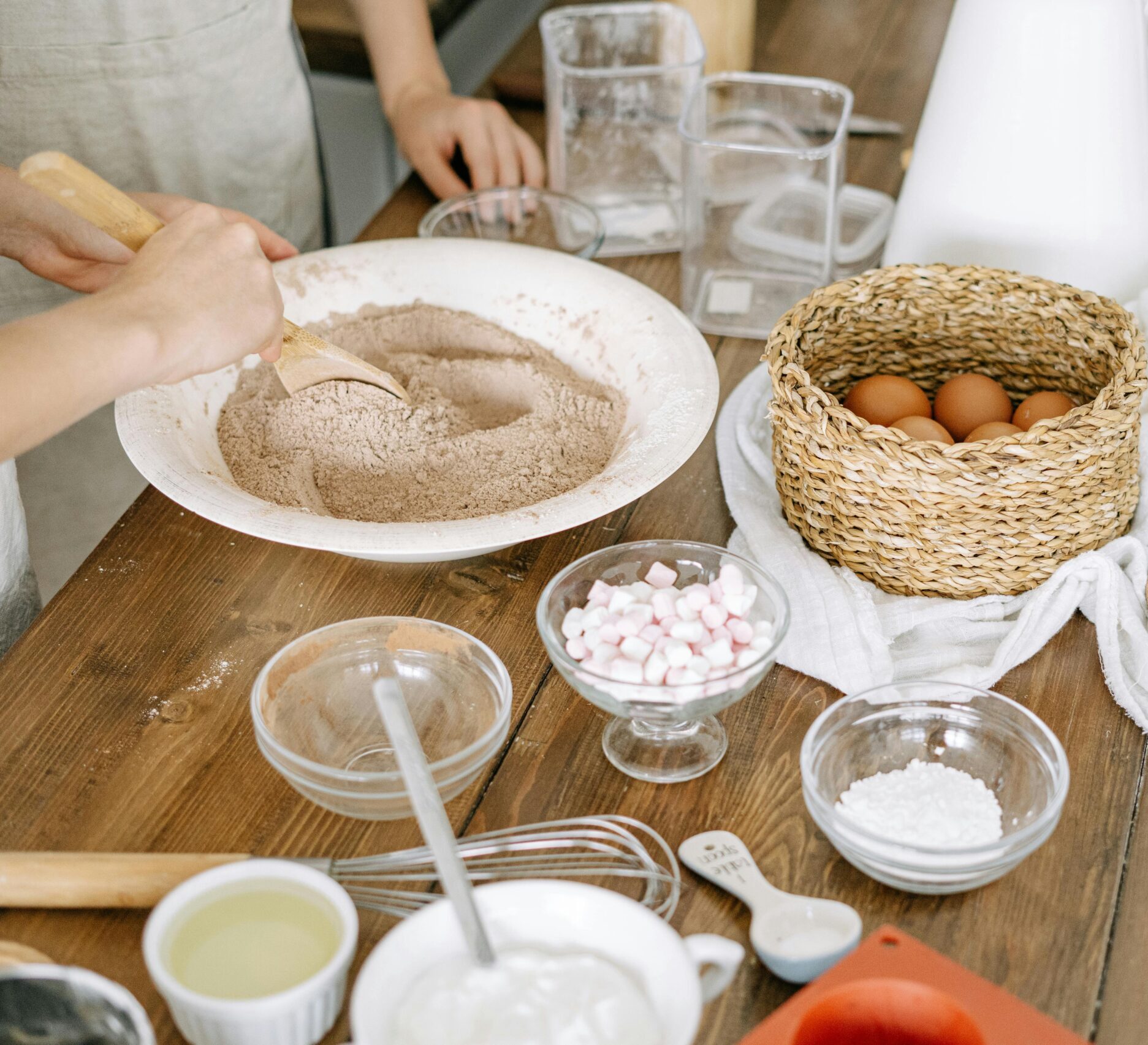Close-up of hands mixing baking ingredients on a wooden table indoors.