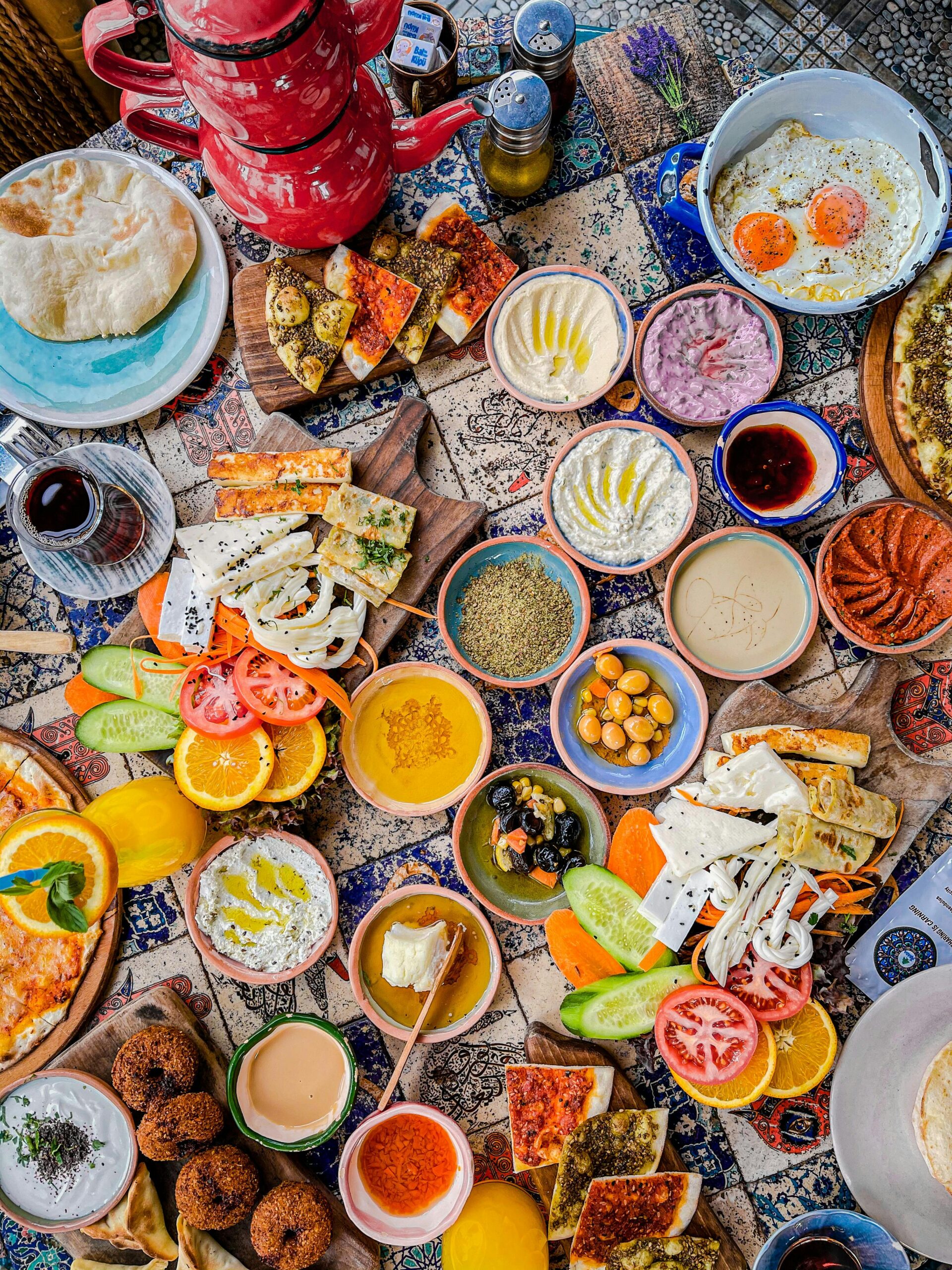 A vibrant flat lay of assorted Mediterranean breakfast dishes on decorated tiles.