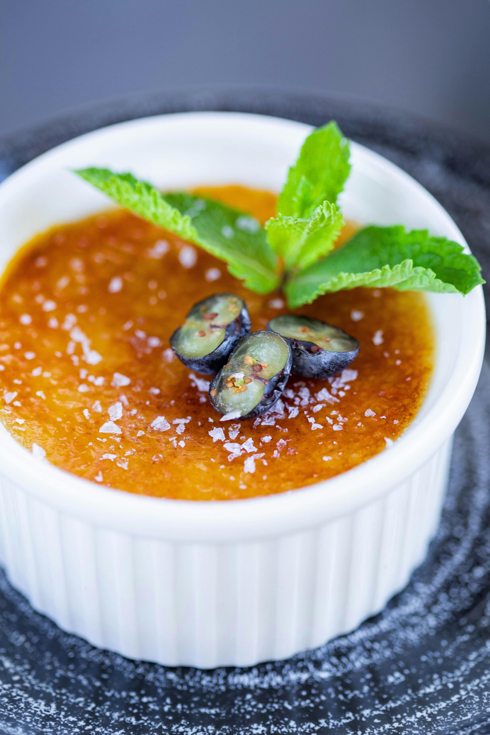 Close-up of a creamy crème brûlée topped with mint and berries.