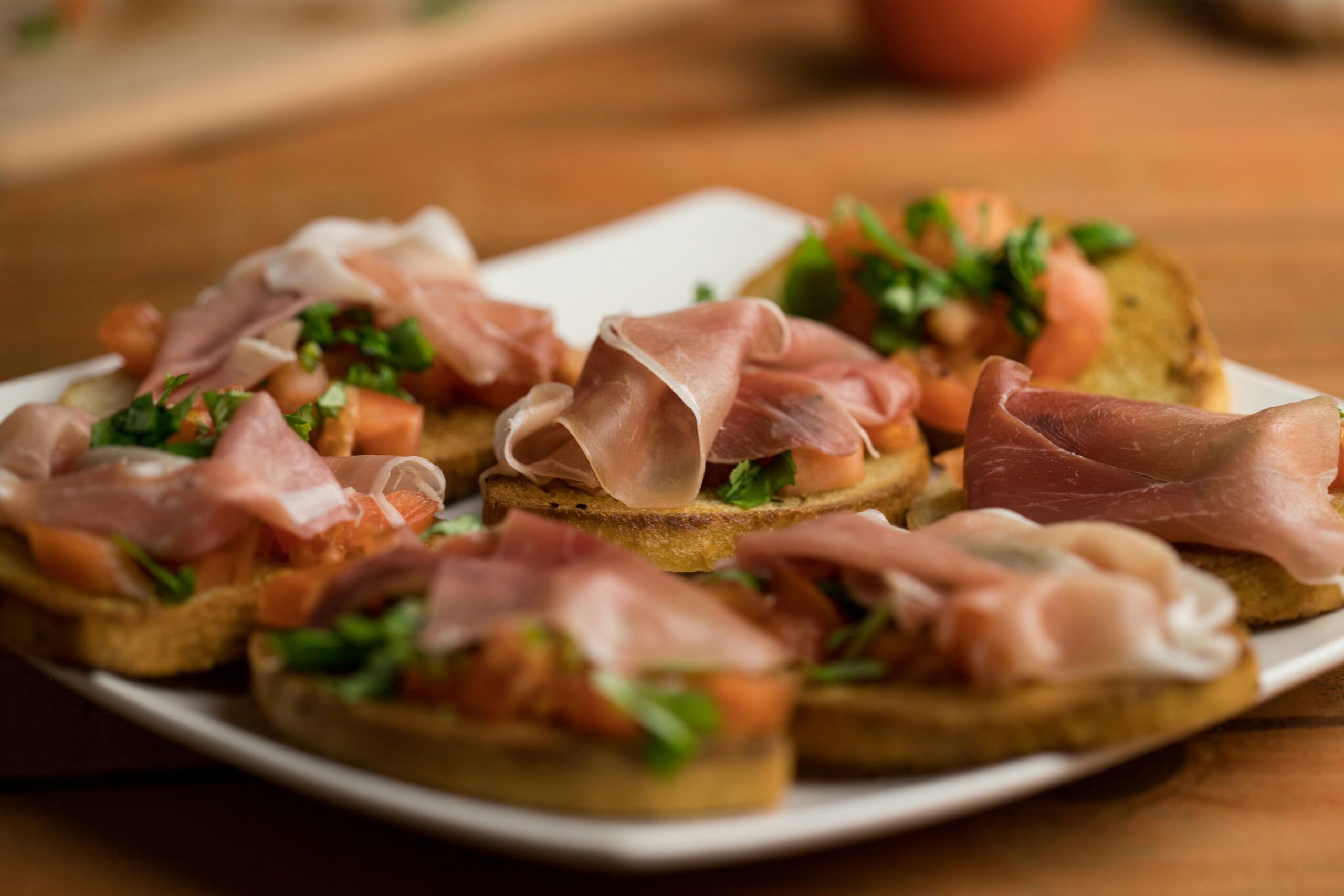 Delicious Italian bruschetta topped with prosciutto and fresh herbs on a wooden table.