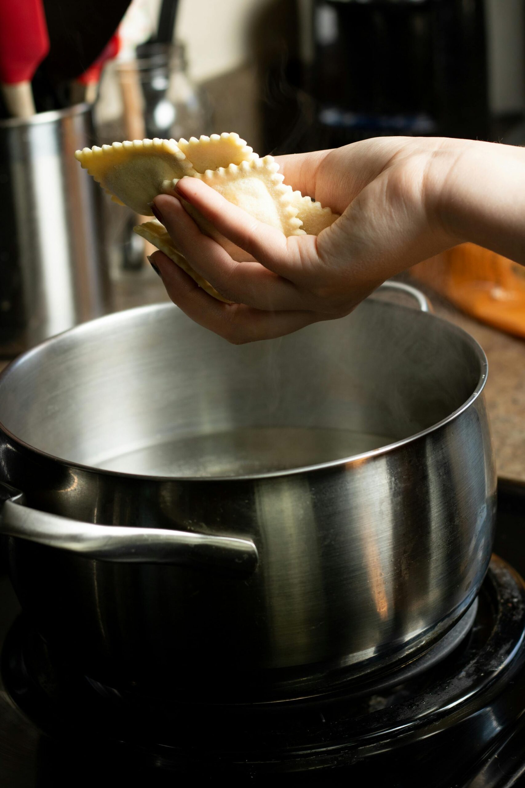 A hand adds fresh ravioli to a boiling pot, highlighting home cooking and culinary freshness.