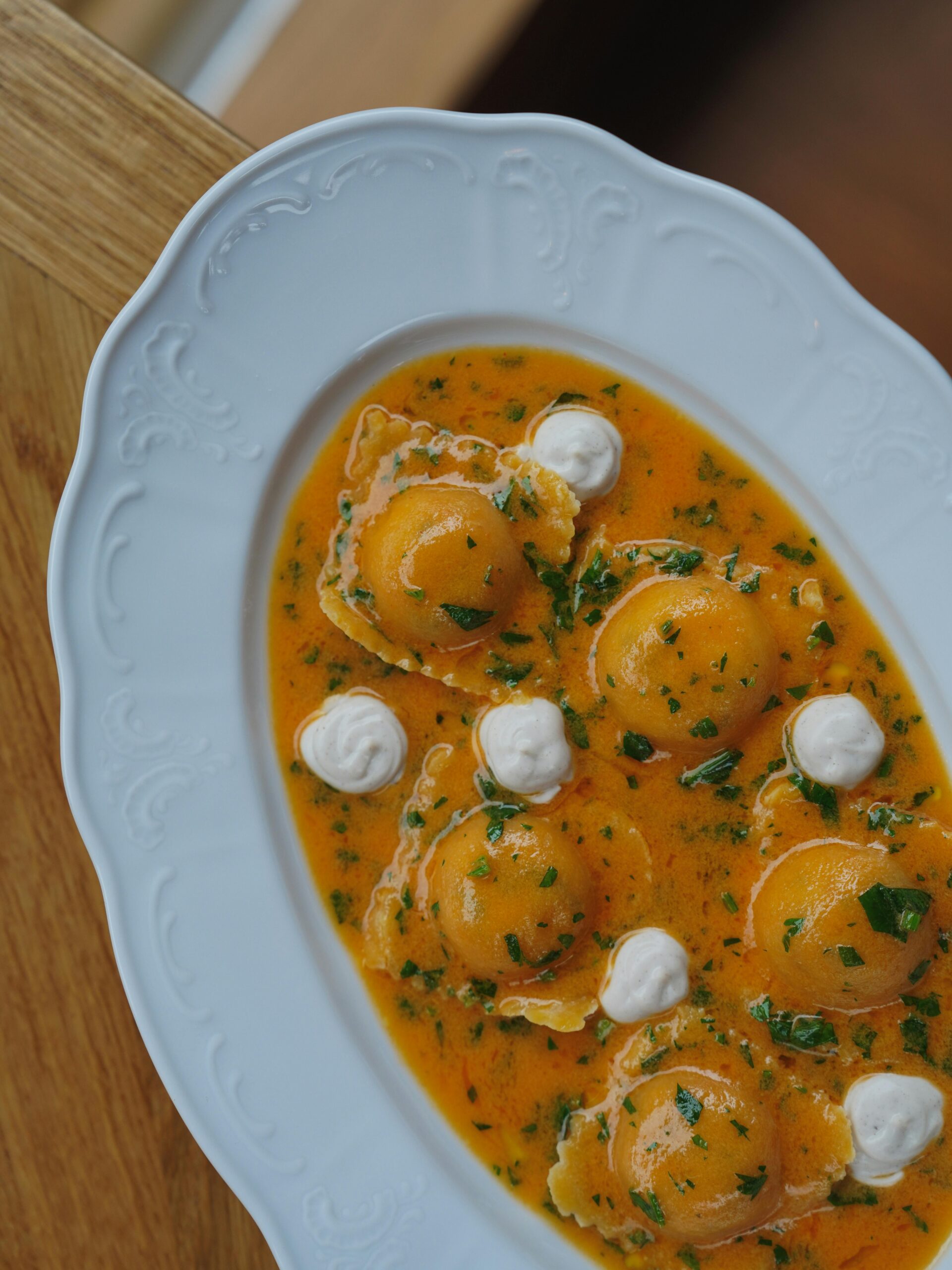 Mouth-watering ravioli served on a white plate with a rich, creamy orange sauce and garnished with herbs.