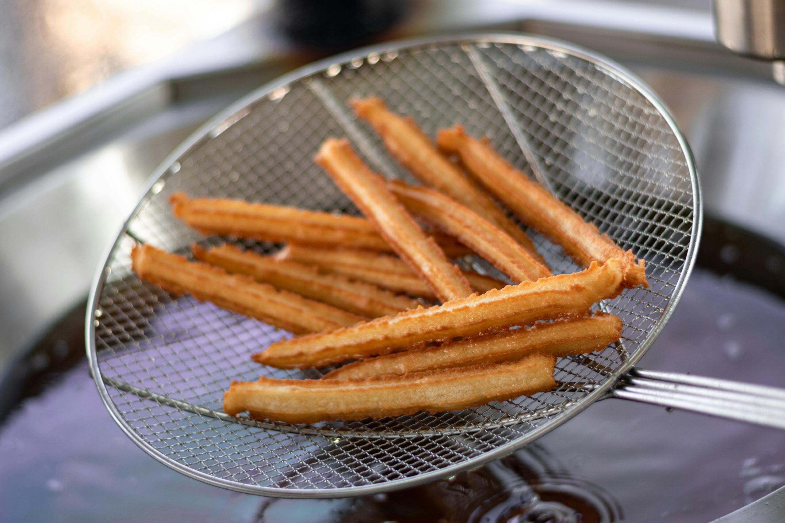 Close-up of freshly fried churros being drained on a wire skimmer, ready to serve.