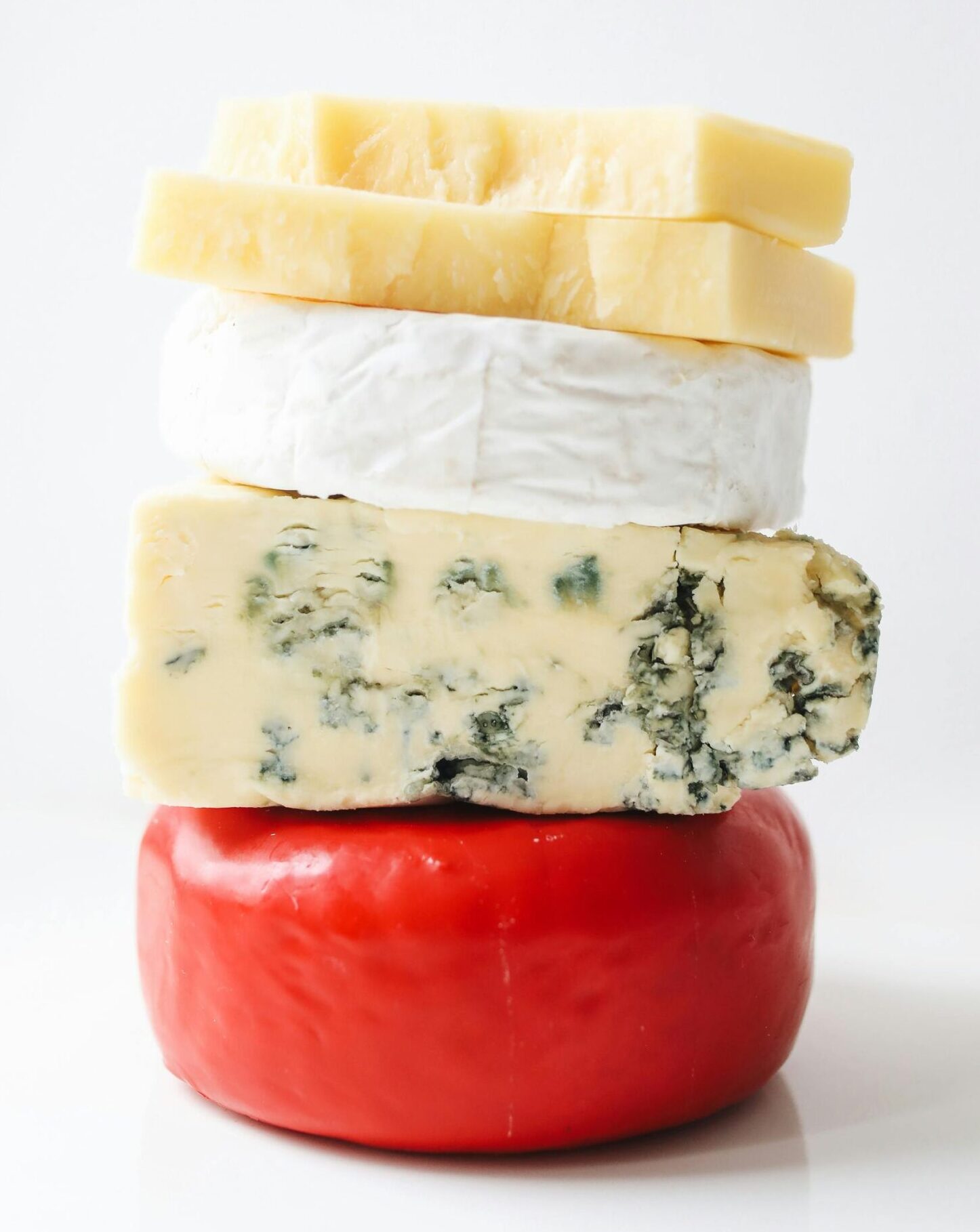 Artistic stack of diverse gourmet cheeses on a white background.