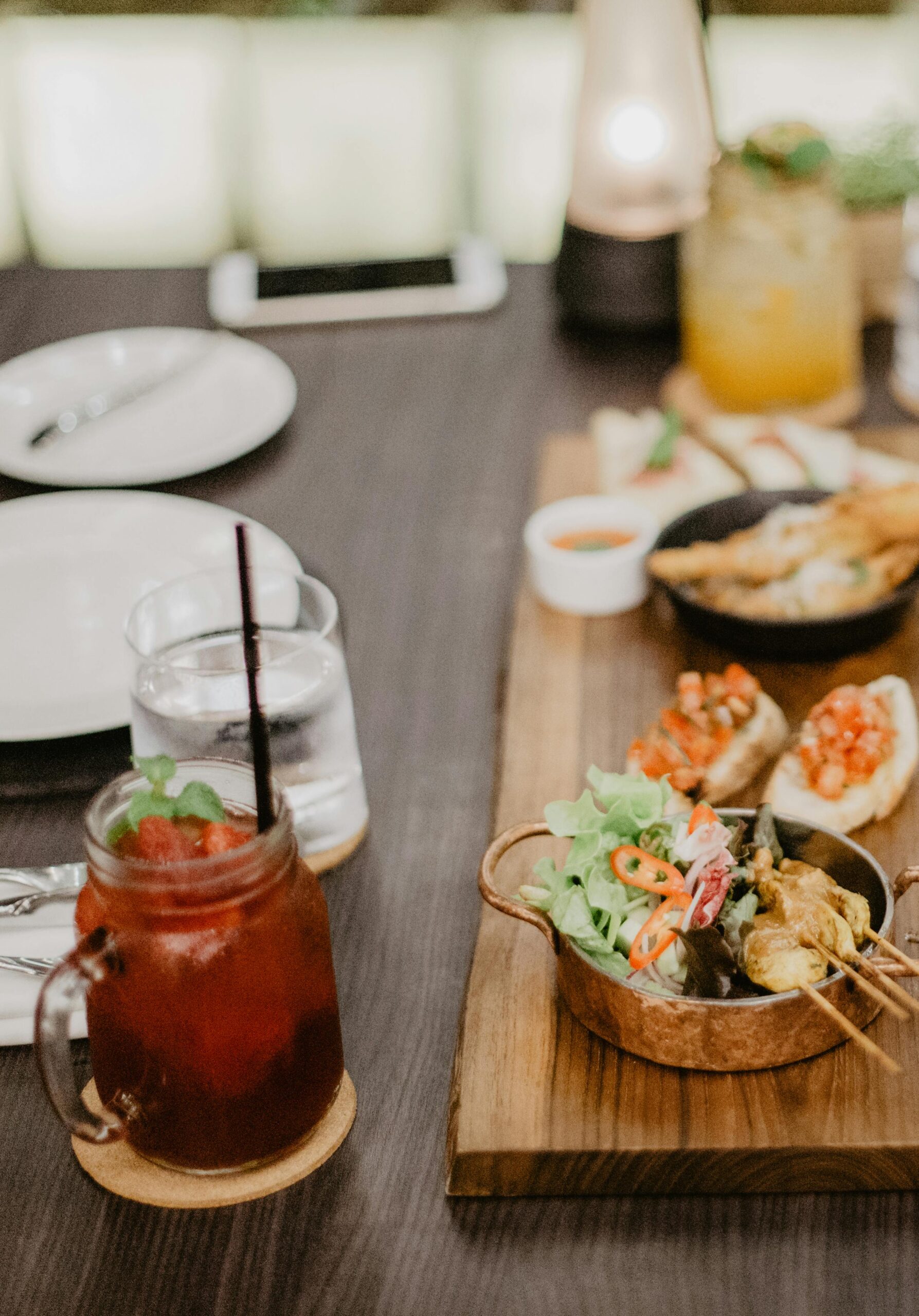 Close-up of gourmet appetizers and refreshing drinks on a wooden board in a cozy café setting.
