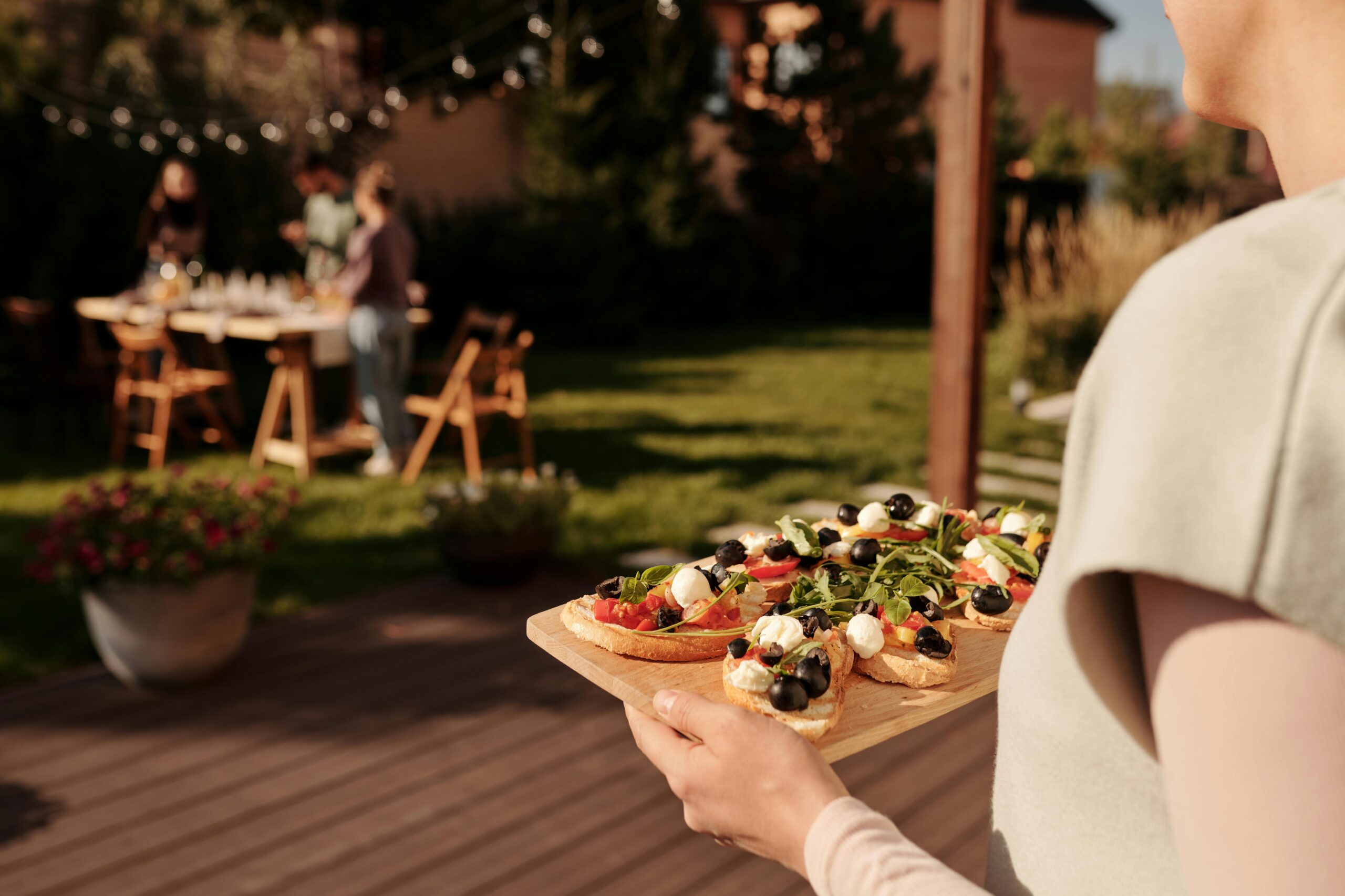 A woman holding a tray of fresh appetizers at an outdoor gathering with friends in a garden setting.