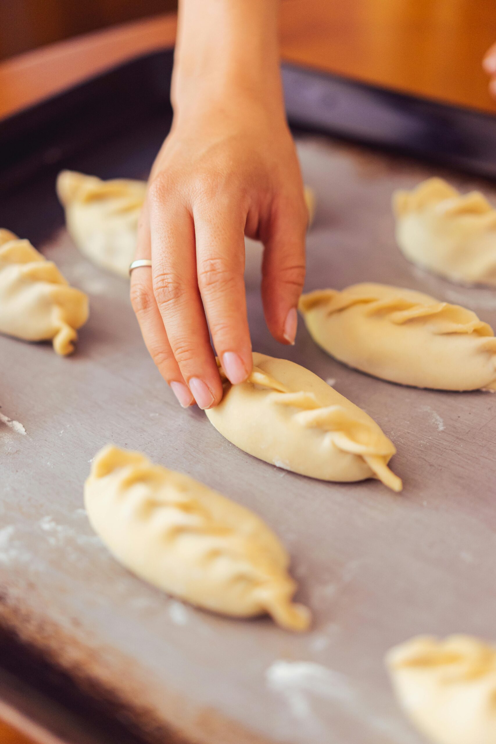 A hand placing homemade empanadas on a baking tray, showcasing traditional food preparation.