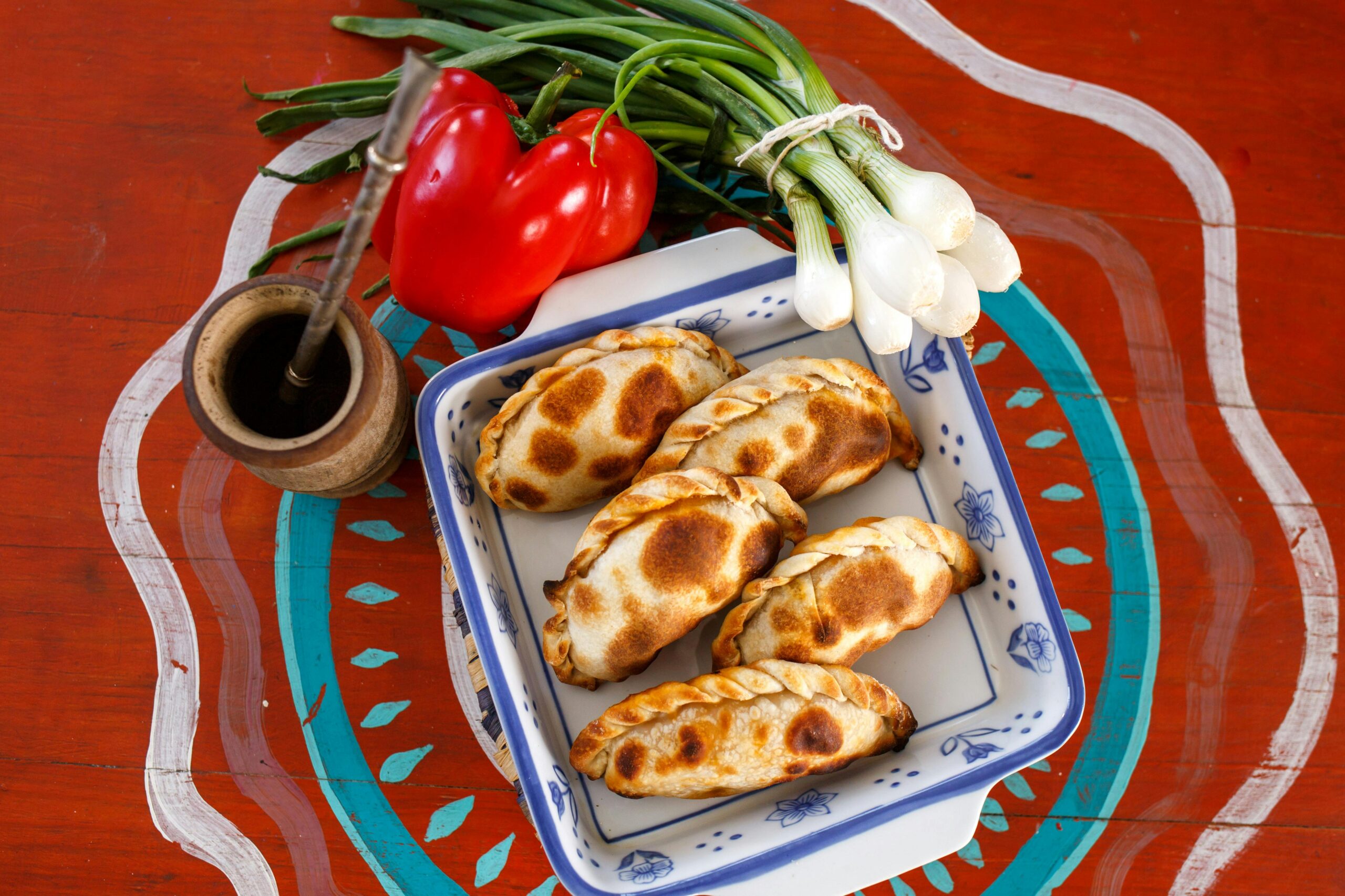 Plate of Argentine empanadas with traditional mate, red pepper, and green onions.