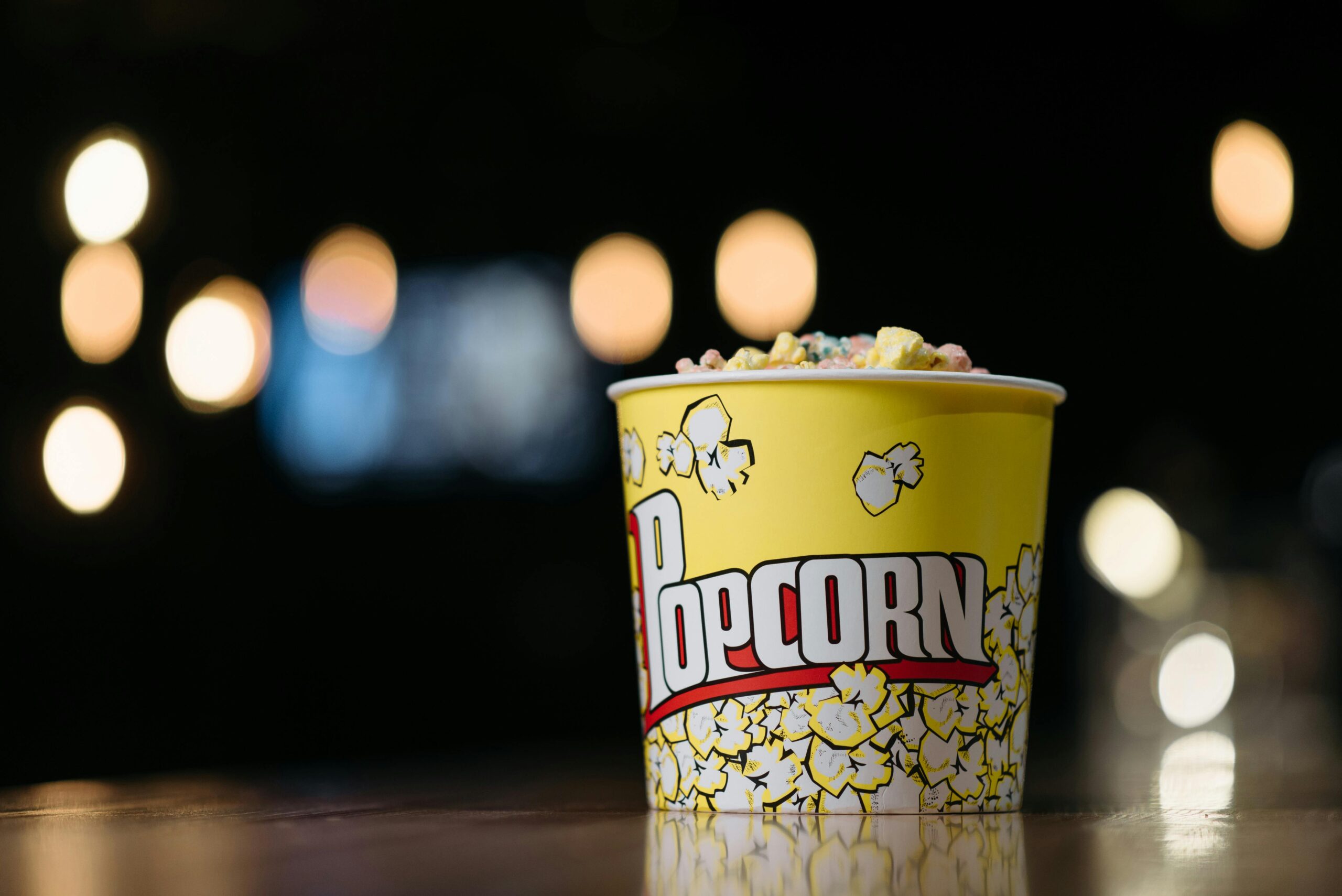 Vibrant yellow popcorn container filled with colorful popcorn against a bokeh background.