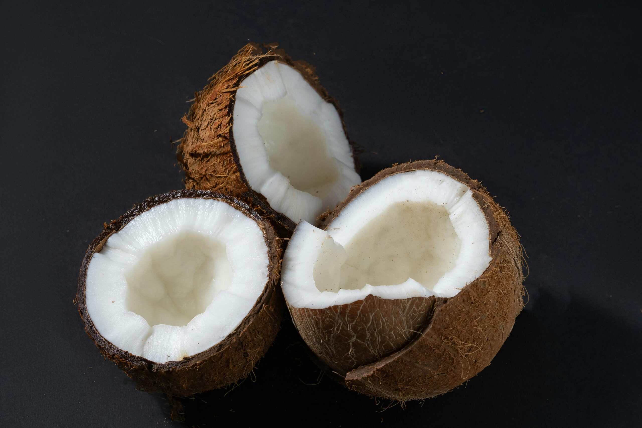 Close-up of three fresh, cracked coconuts on a black background.
